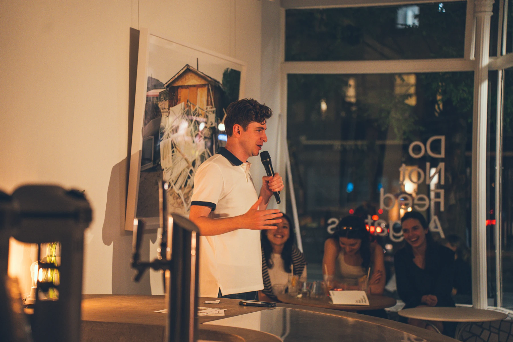 Ryan Beck holding a microphone beside the audience in a small comedy venue.